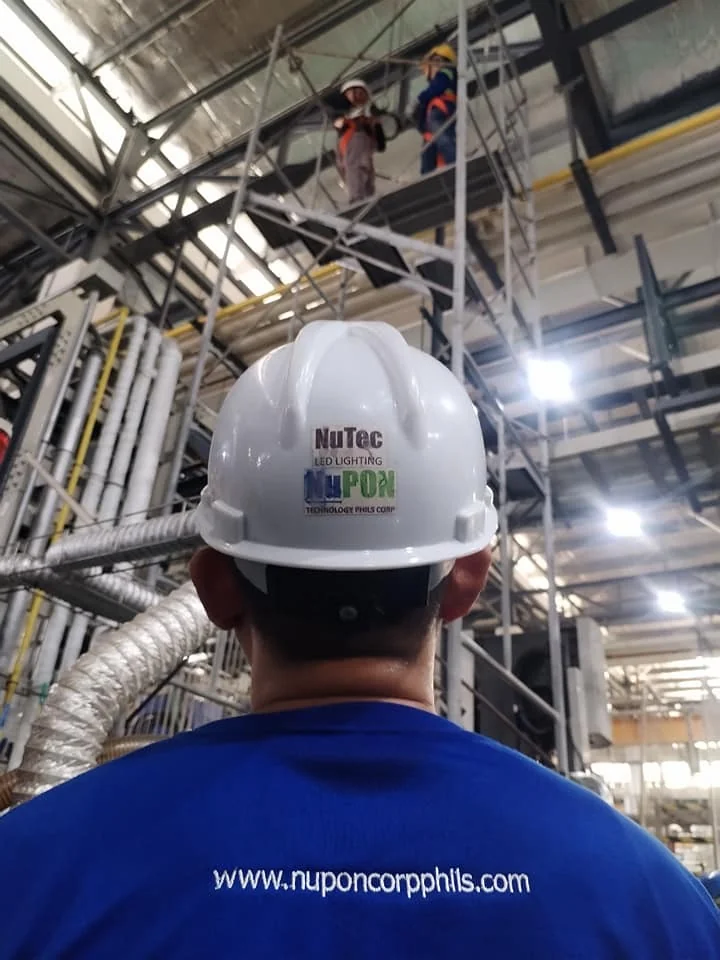 technician-factory-site.webp A NuPON technician in a NuTec LED Lighting branded hard hat watching colleagues work on a scaffold inside a factory.